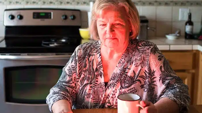 mature woman sitting at the table and sipping hot cup of coffee whle enjoing dry skin in winter remedies: red light therapy and learning - how to take care of skin in winter naturally