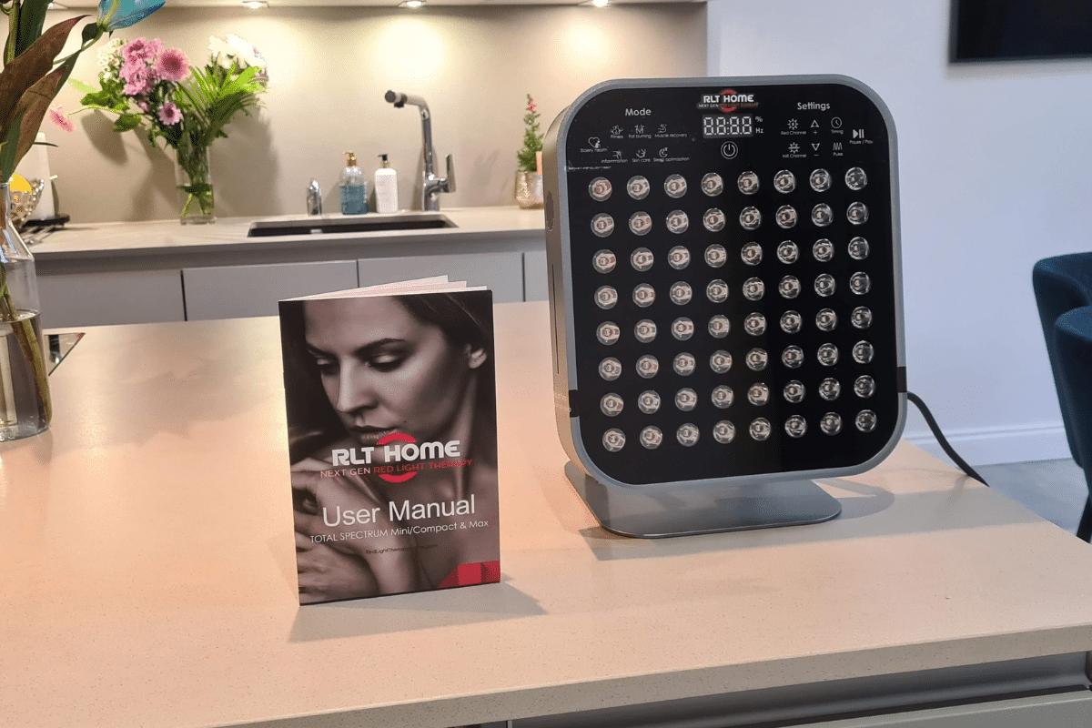 Total Spectrum MINI red light therapy device on a kitchen counter next to the user manual